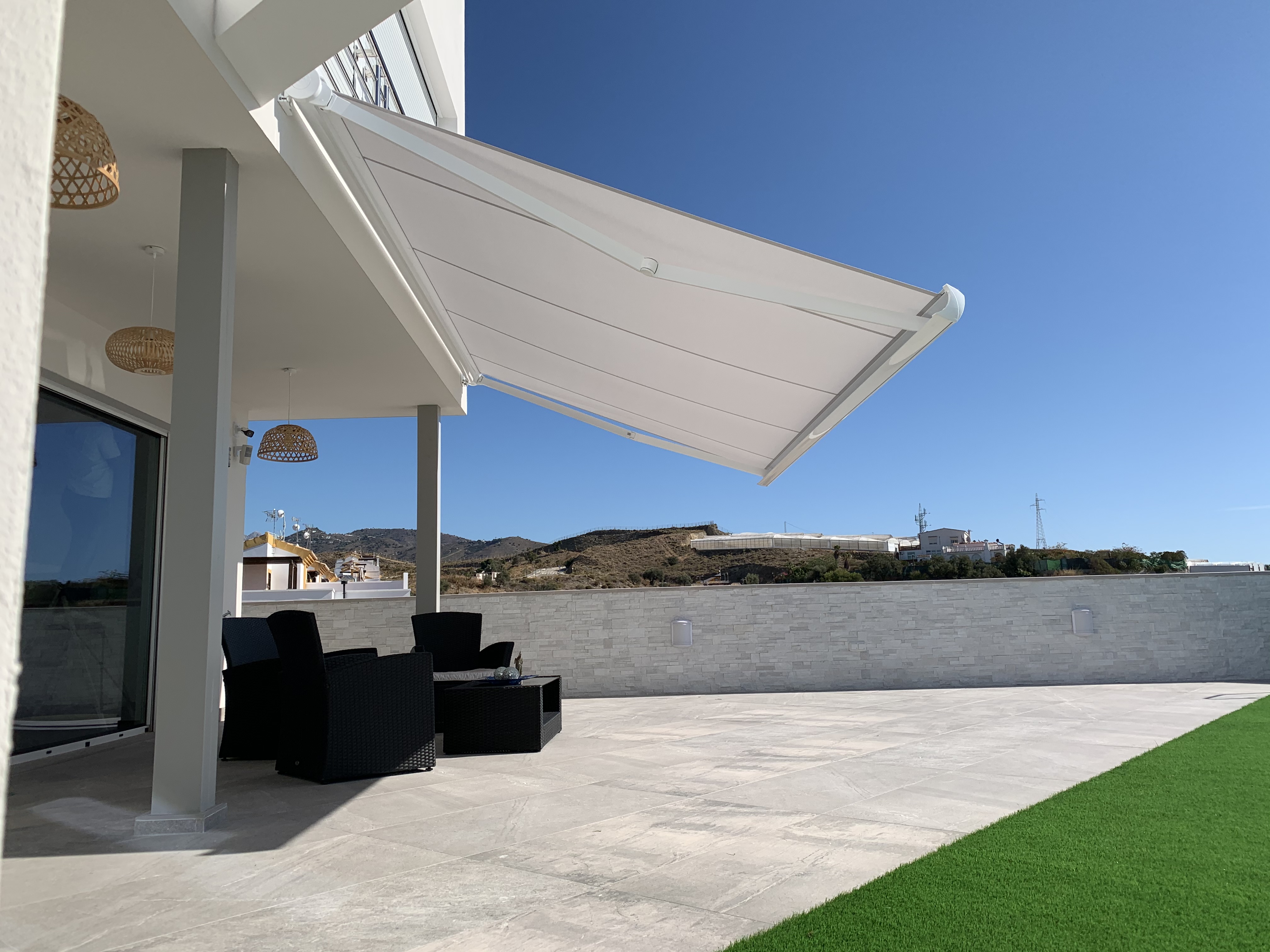 Toldo retráctil blanco sobre terraza con mobiliario exterior y cielo azul - Servitoldos Daniel